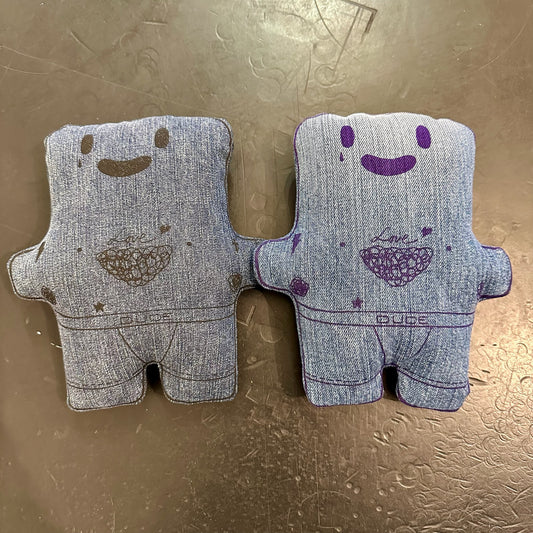 Two plush, denim-like figures with smiling faces and heart patterns on a textured surface.